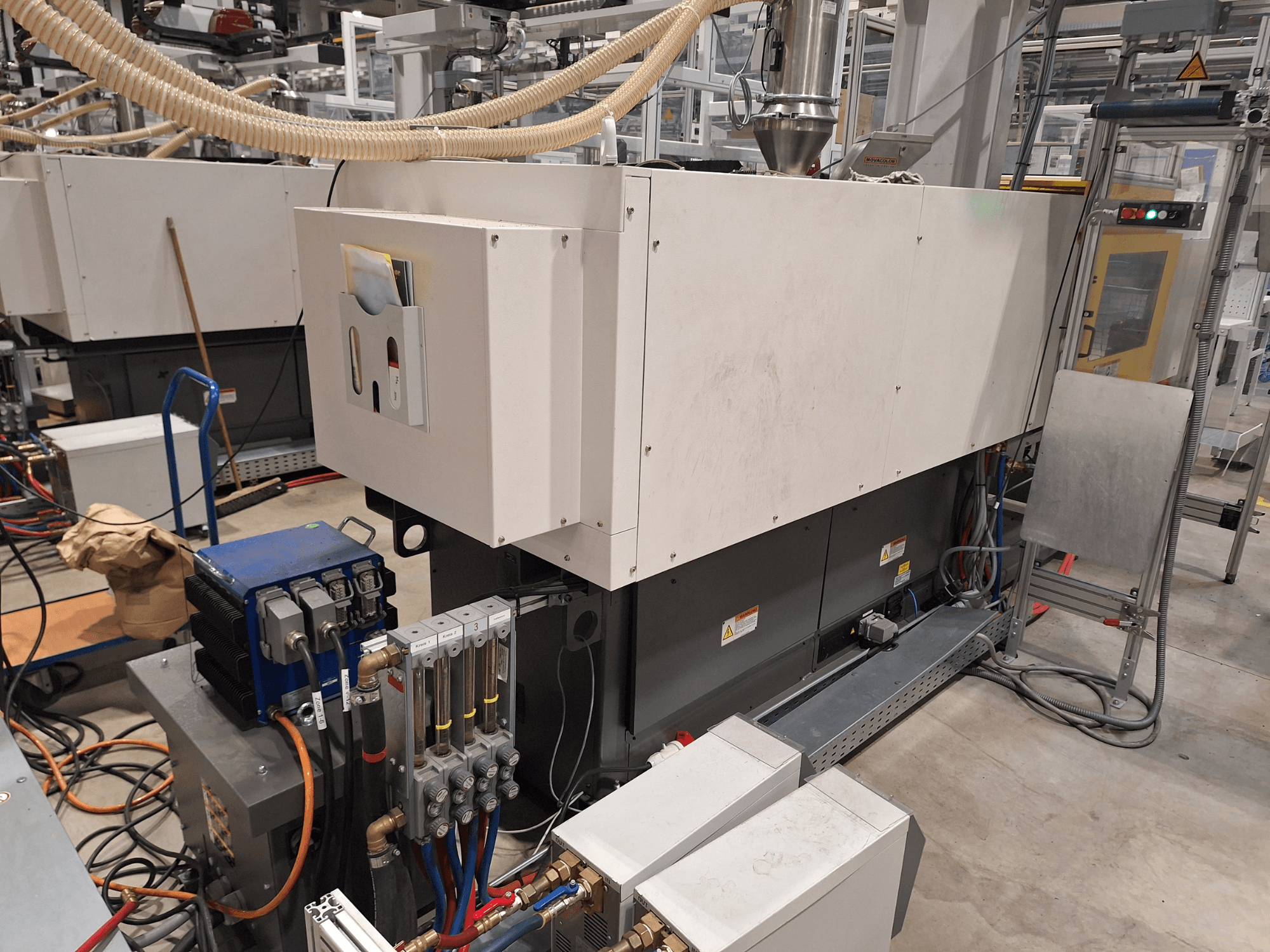 Rūpnieciskās iekārtas rūpnīcā; ietver lielu mašīnu ar vadības paneli, šļūtenēm un elektrības savienojumiem, skats no malas.