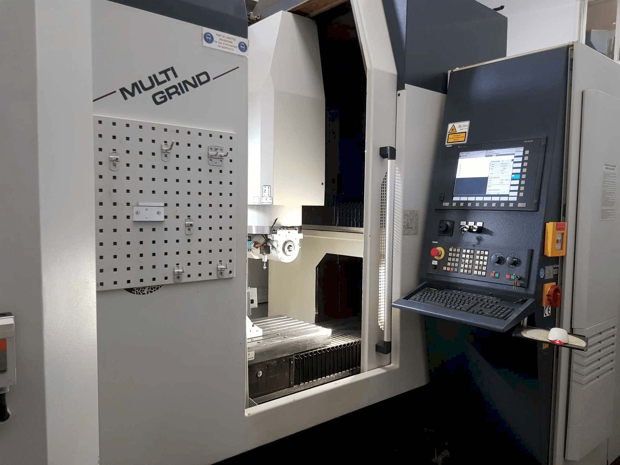 Multi Grind CNC slīpmašīna ar skatu no priekšpuses, kurā ir vadības panelis, uzglabāšanas pegboard un atvērta darba zona.
